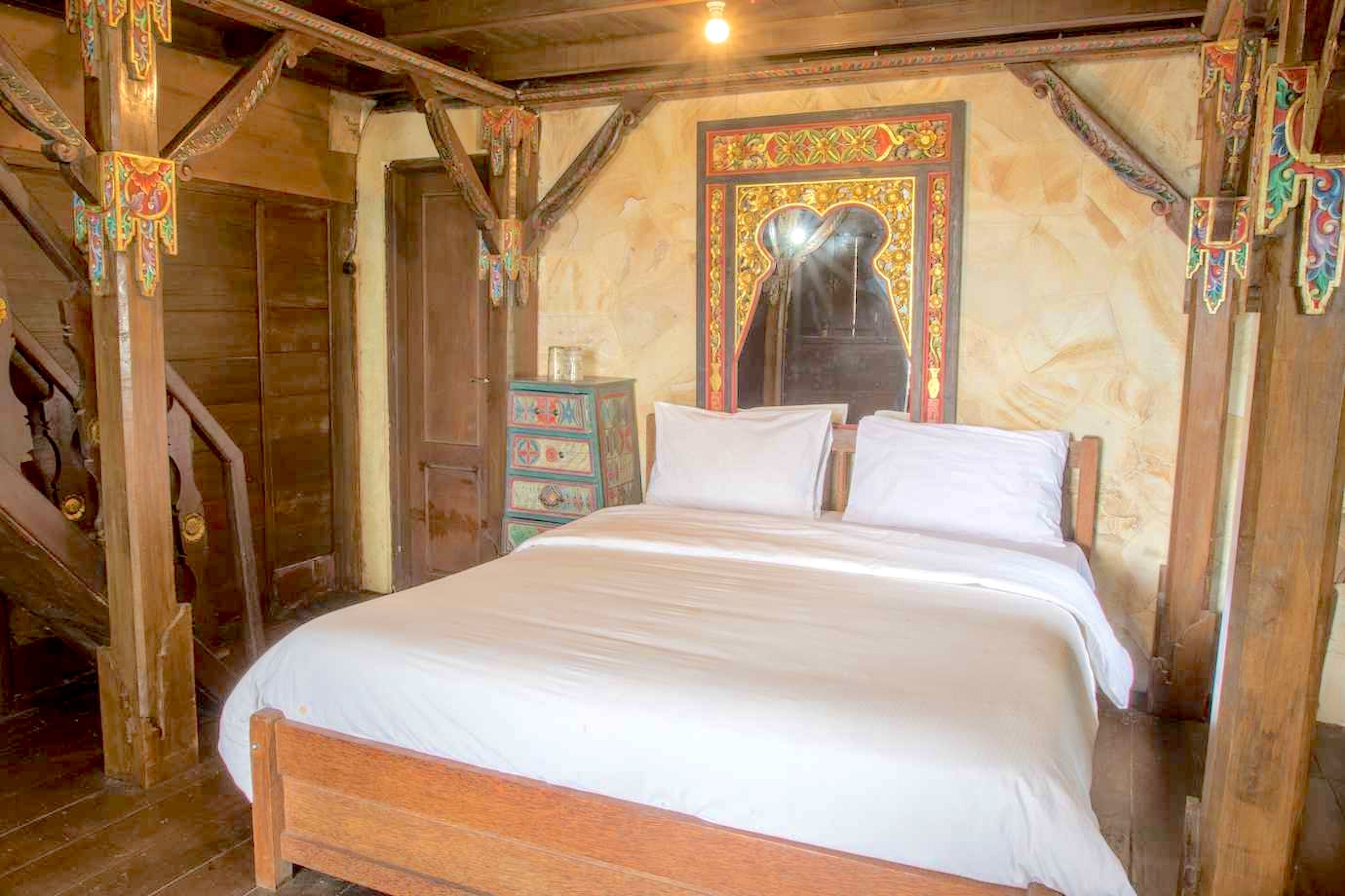 A wooden room with a bed, a chest of drawers, and a staircase.