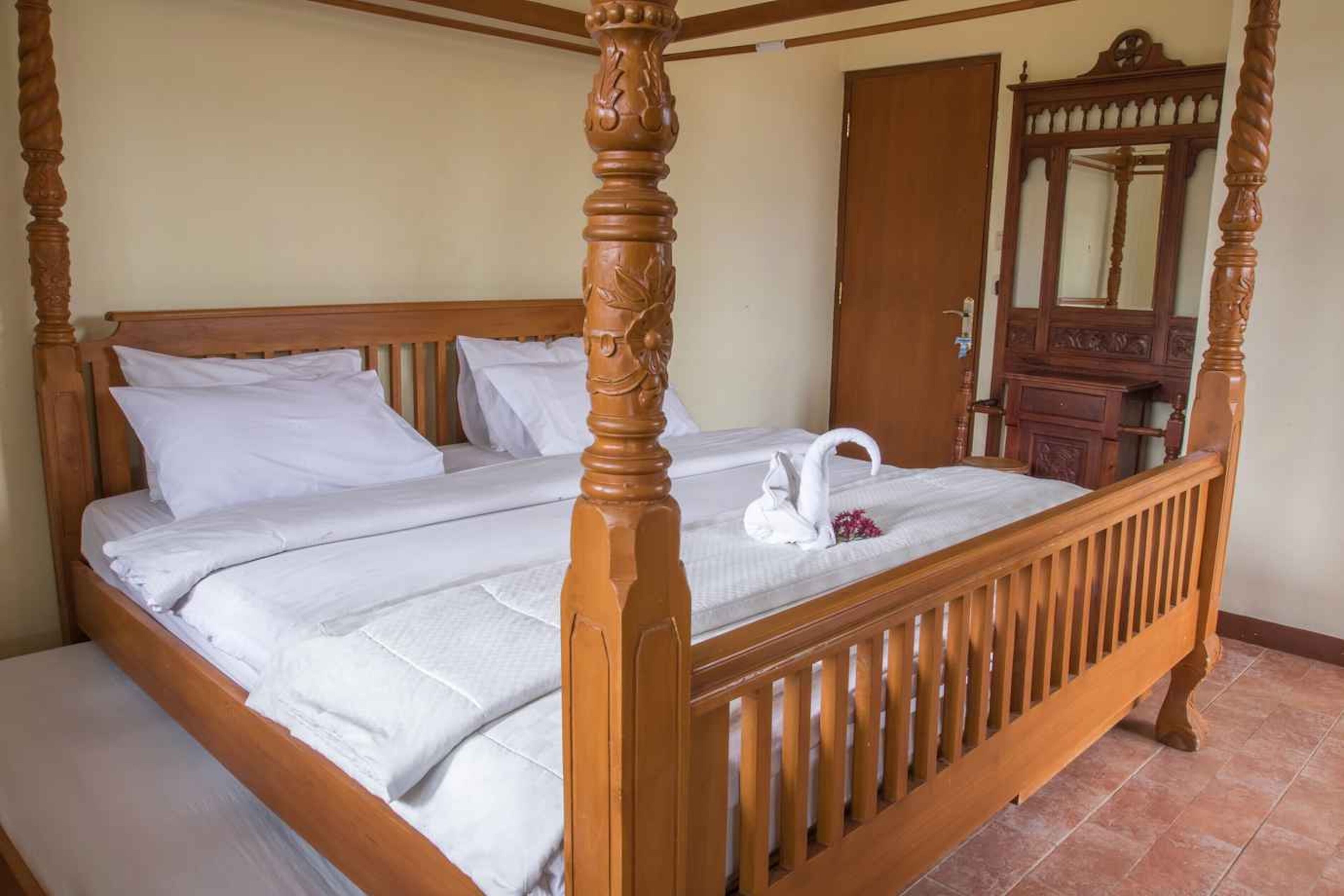 Una cama con dosel, ropa de cama blanca, cabecera de madera y una mesita de noche con espejo.