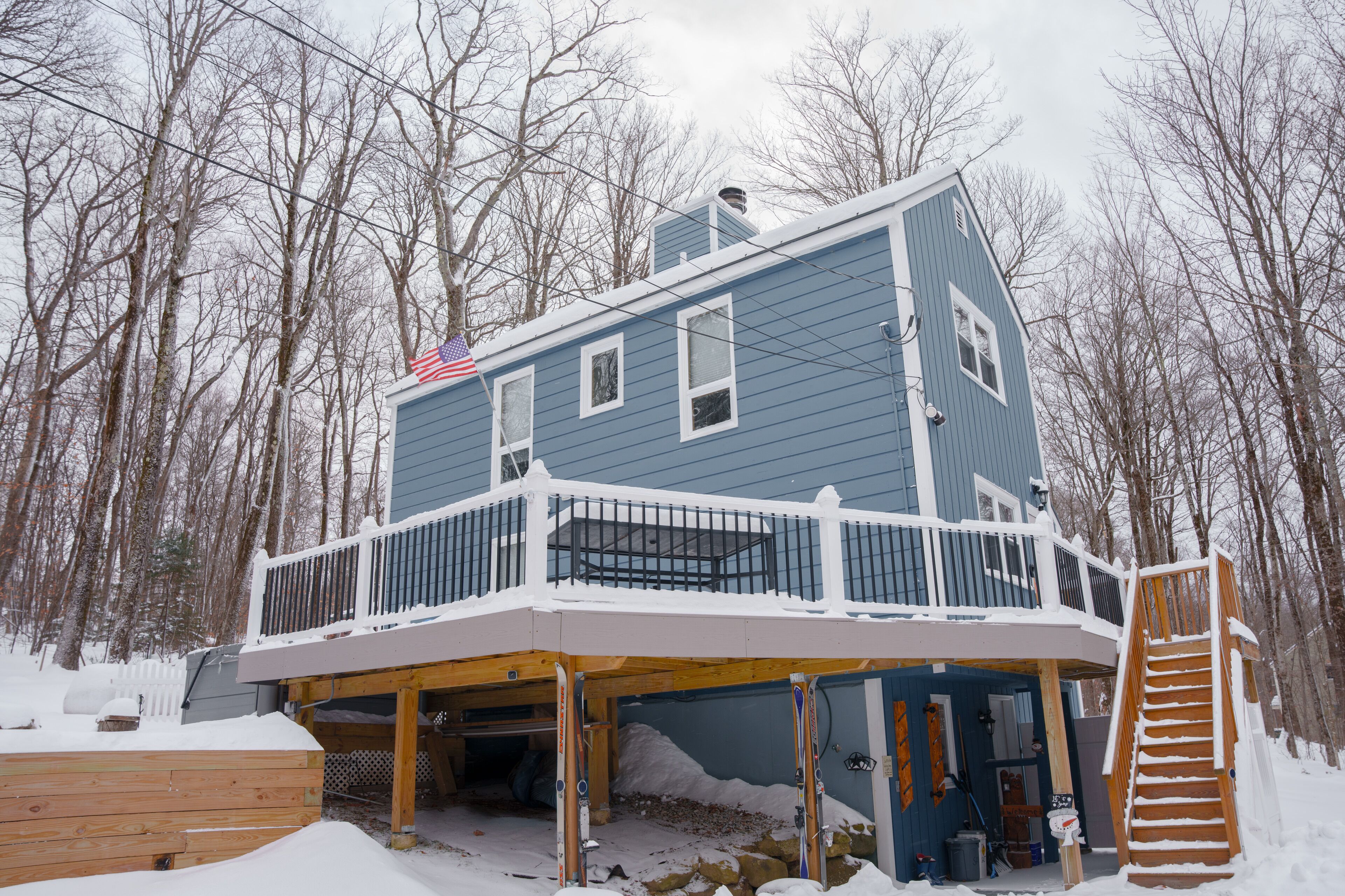 Une maison à deux étages avec un balcon et une terrasse, entourée d’arbres et recouverte de neige.