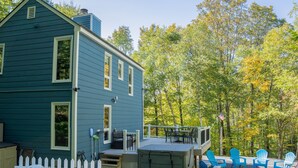 Una casa azul con terraza, mobiliario exterior y vistas a un bosque.