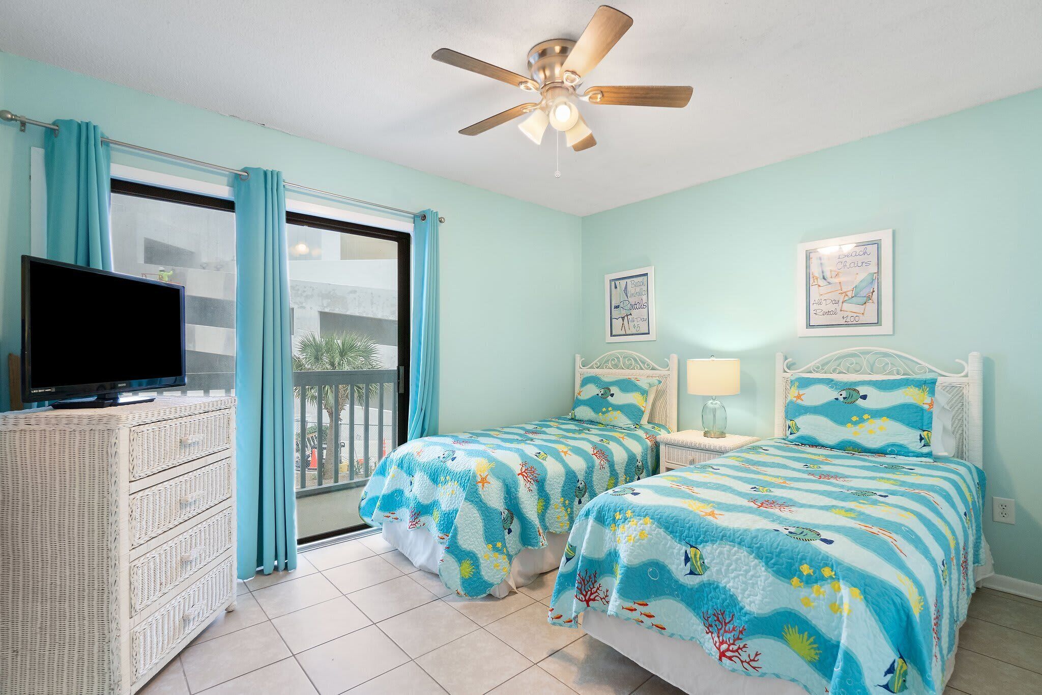 A bedroom with two beds, a TV, a ceiling fan, and a balcony.