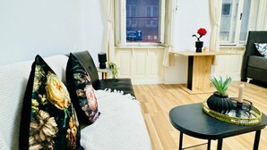 Un salon avec un canapé, une petite table sur laquelle se trouvent un vase et une bougie, et une fenêtre avec des rideaux.