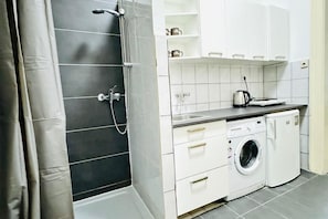 Cocina compacta con lavadora, cafetera y zona de ducha.