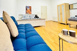 A modern room with a blue sofa, a small table with two mugs, a cabinet, and a painting on the wall.