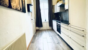 A narrow kitchen with a radiator, a window with curtains, and a stove.
