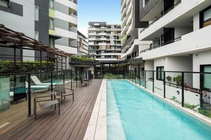 A modern apartment building with a rooftop swimming pool, outdoor seating, and a view of the surrounding buildings. - Charming 2BDR Nundah Stay with Golden Sunsets (Nundah)