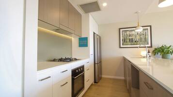 A modern kitchen with white cabinetry, a gas stove, a built-in oven, a stainless steel refrigerator, and a sink.