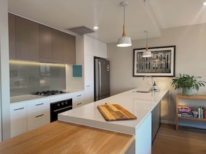 Una cucina moderna con mobili bianchi, un frigorifero in acciaio inossidabile, un piano di lavoro in legno e illuminazione a sospensione.