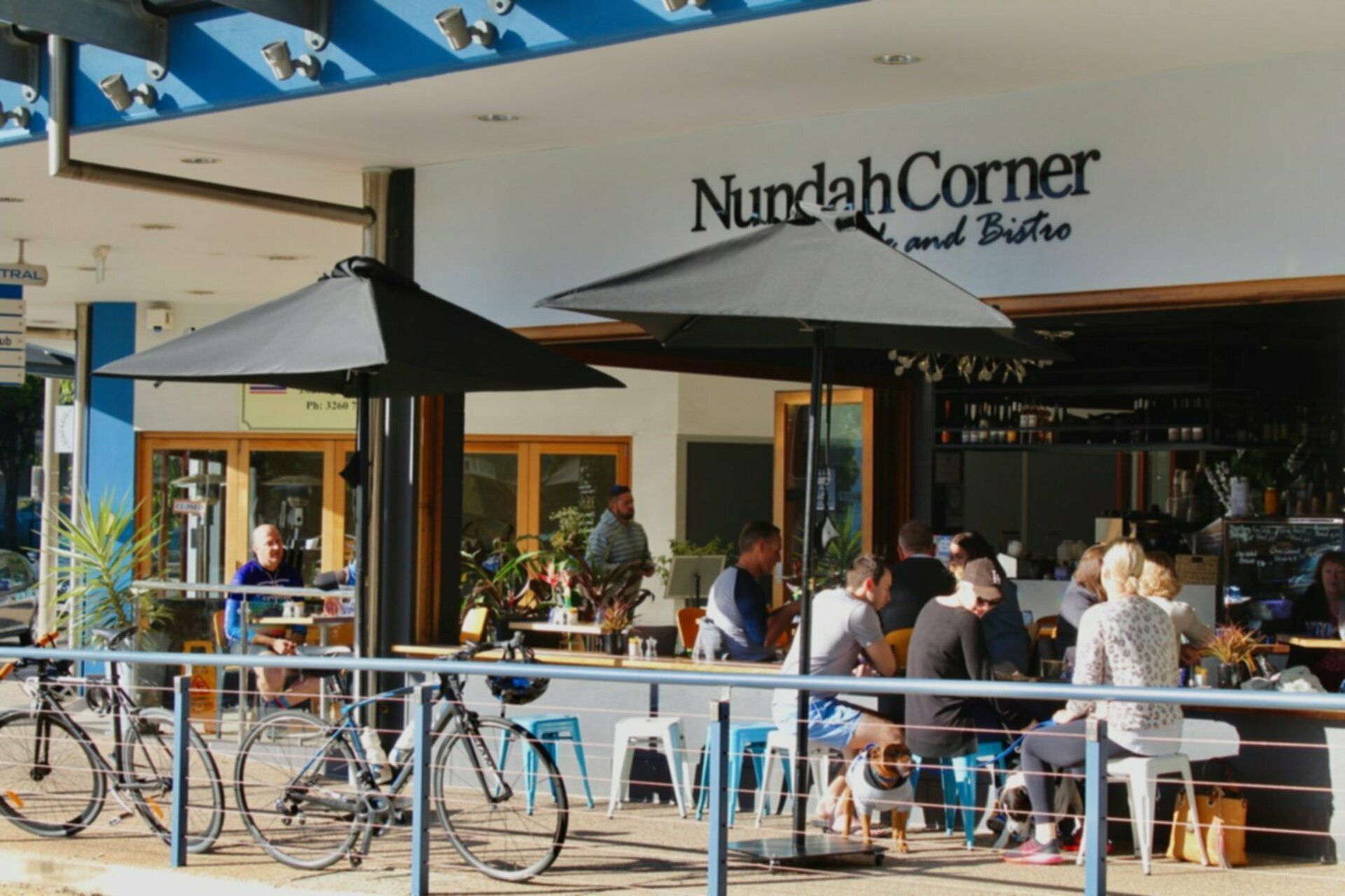 An outdoor seating area with umbrellas, bicycles, and a sign for 'Nundah Corner and Bistro'.