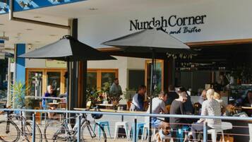 An outdoor seating area with umbrellas, bicycles, and a sign for 'Nundah Corner and Bistro'.