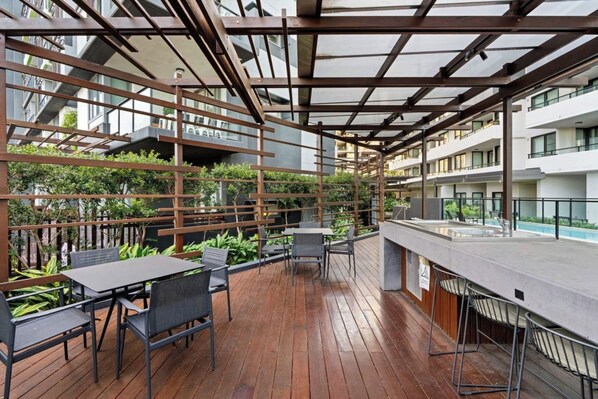 An outdoor patio area with wooden flooring, metal chairs, and tables. - Charming 2BDR Nundah Stay with Golden Sunsets (Nundah)
