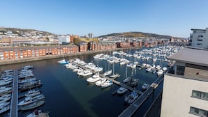 A marina with numerous boats docked, a clear sky, and buildings in the background. - Just Stay Wales Beautiful 1 Bed Flat - Marina View (Swansea)