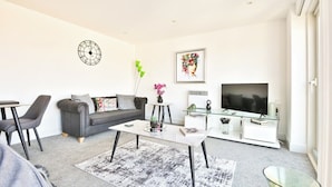 A modern living room with a sofa, coffee table, TV, and decorative items. - Just Stay Wales Beautiful 1 Bed Flat - Marina View (Swansea)