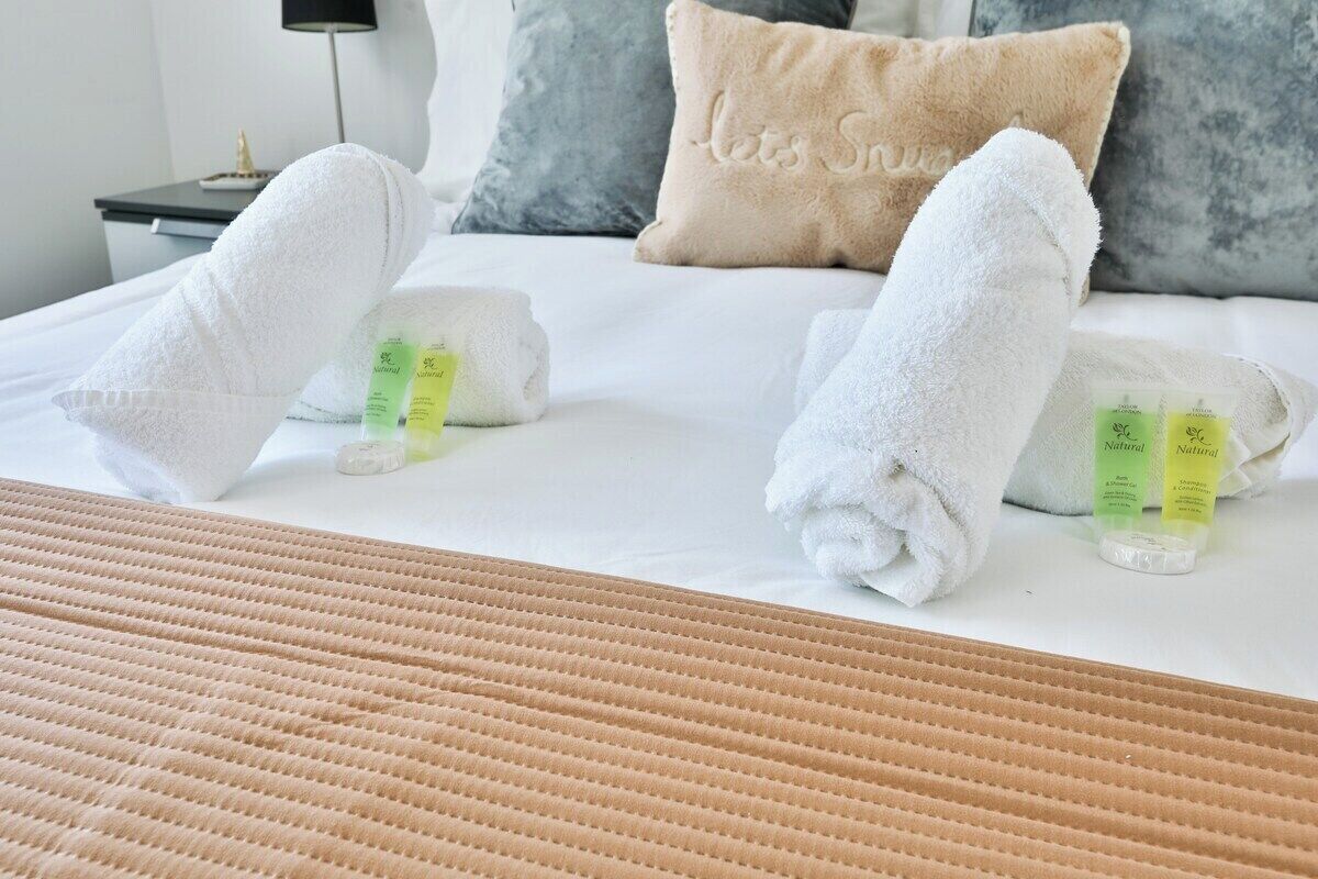 Een net opgemaakt bed met twee witte handdoeken erover gevouwen, een bamboe mat en een nachtkastje met een lamp en een klein decoratief object.