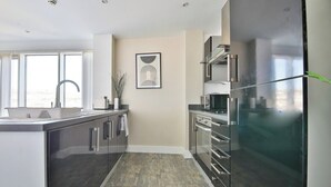 A modern kitchen with a large island, stainless steel appliances, and a view to the outside. - Just Stay Wales Beautiful 1 Bed Flat - Marina View (Swansea)
