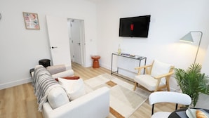 A modern living room with a sofa, armchairs, a coffee table, and a TV mounted on the wall. - Modern & Cosy 2 Bed Flat in Charming Roath (Cardiff)