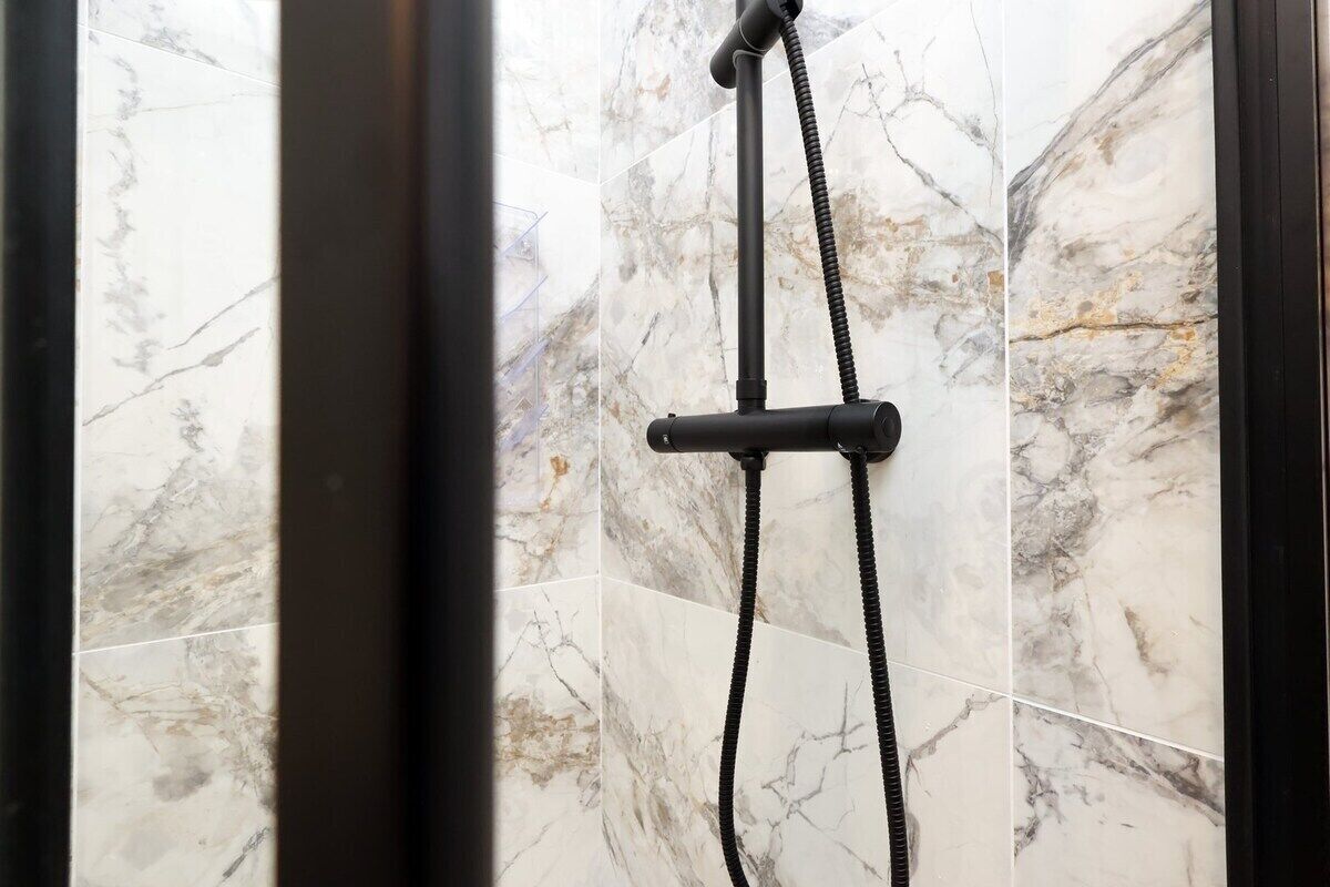 A shower with a handheld hose, set against a marble wall.