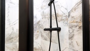 A shower with a black hose and a control bar, set against marble tiles. - Modern & Cosy 2 Bed Flat in Charming Roath (Cardiff)