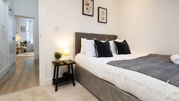 A bedroom with a bed, bedside table, lamp, and two framed pictures on the wall. - Modern & Cosy 2 Bed Flat in Charming Roath (Cardiff)