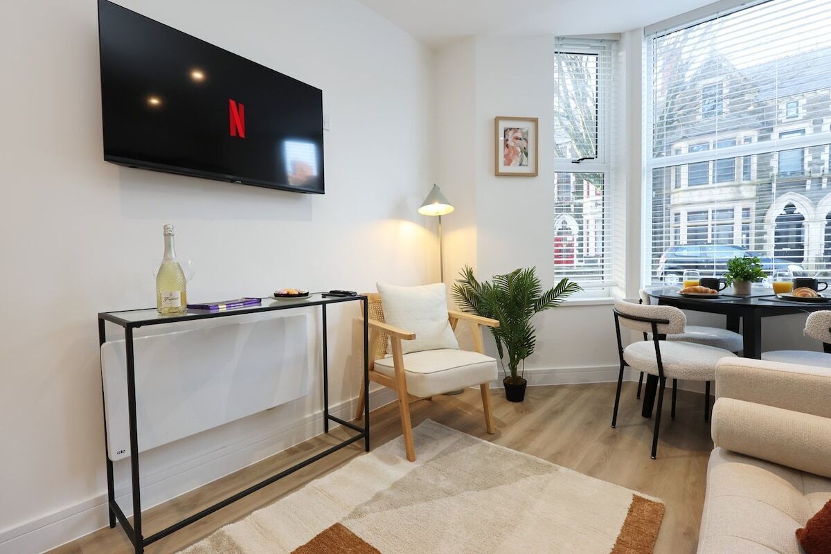 Un salon moderne doté d’un téléviseur à écran plat, d’une table à manger, de chaises, d’un canapé, d’une plante en pot et d’une fenêtre offrant une vue sur les bâtiments.