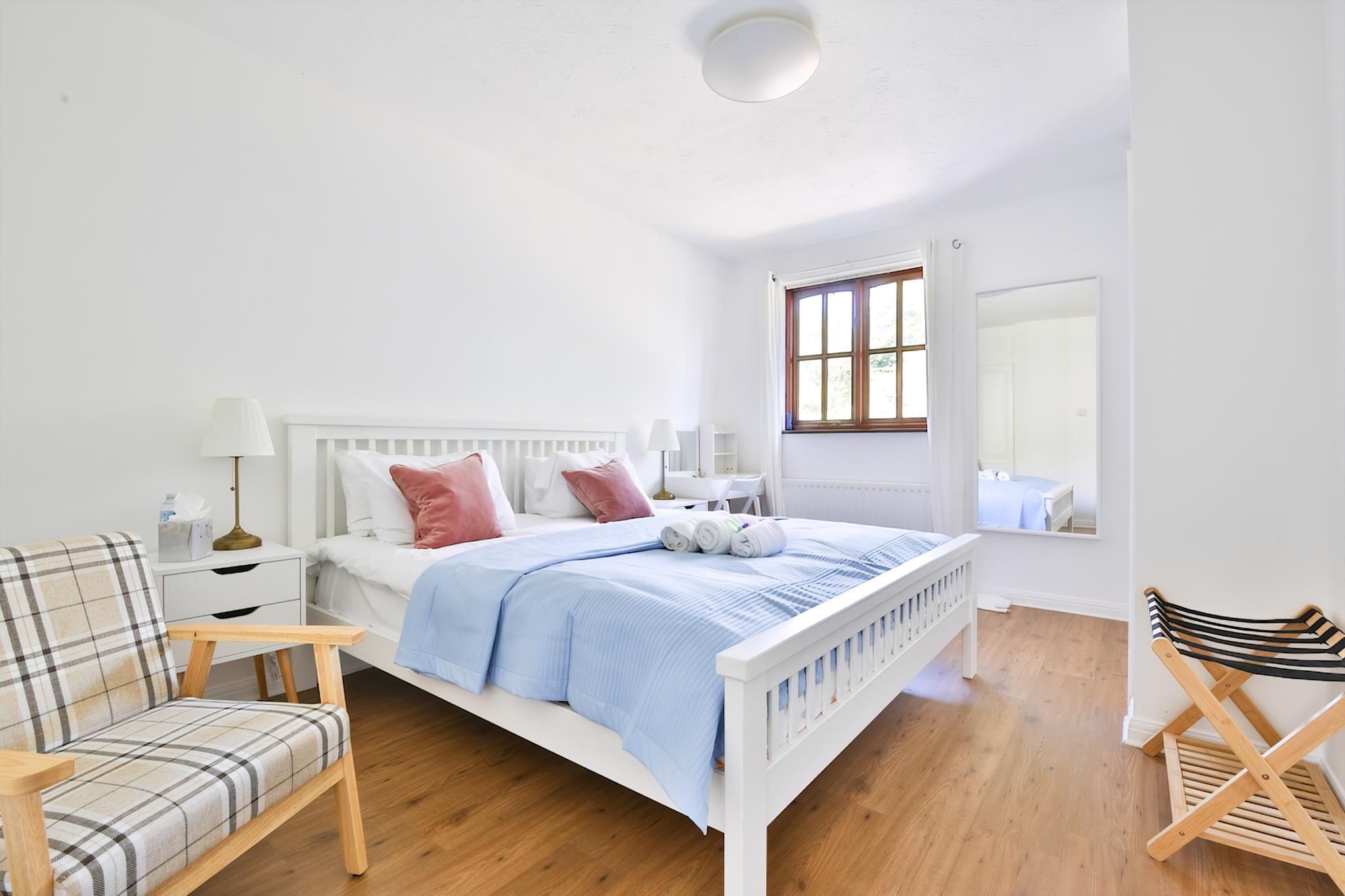 A bedroom with a white bed, a chair, a small table, and a mirror.