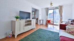 Un salon équipé d’un téléviseur à écran plat, d’un meuble, d’un tapis vert, d’un canapé rouge et offrant une vue sur l’extérieur à travers une porte vitrée.