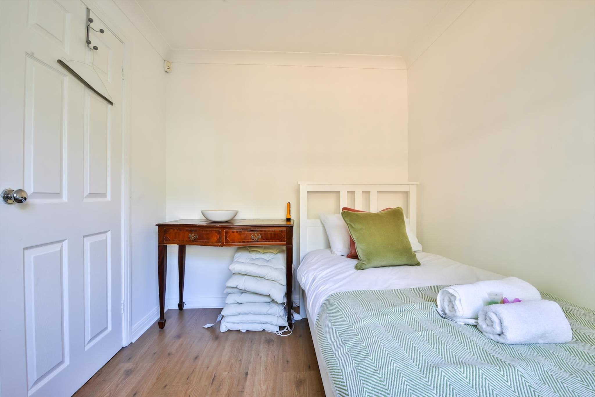 A bedroom with a bed, pillows, a bedside table with a bowl, and a stack of towels.
