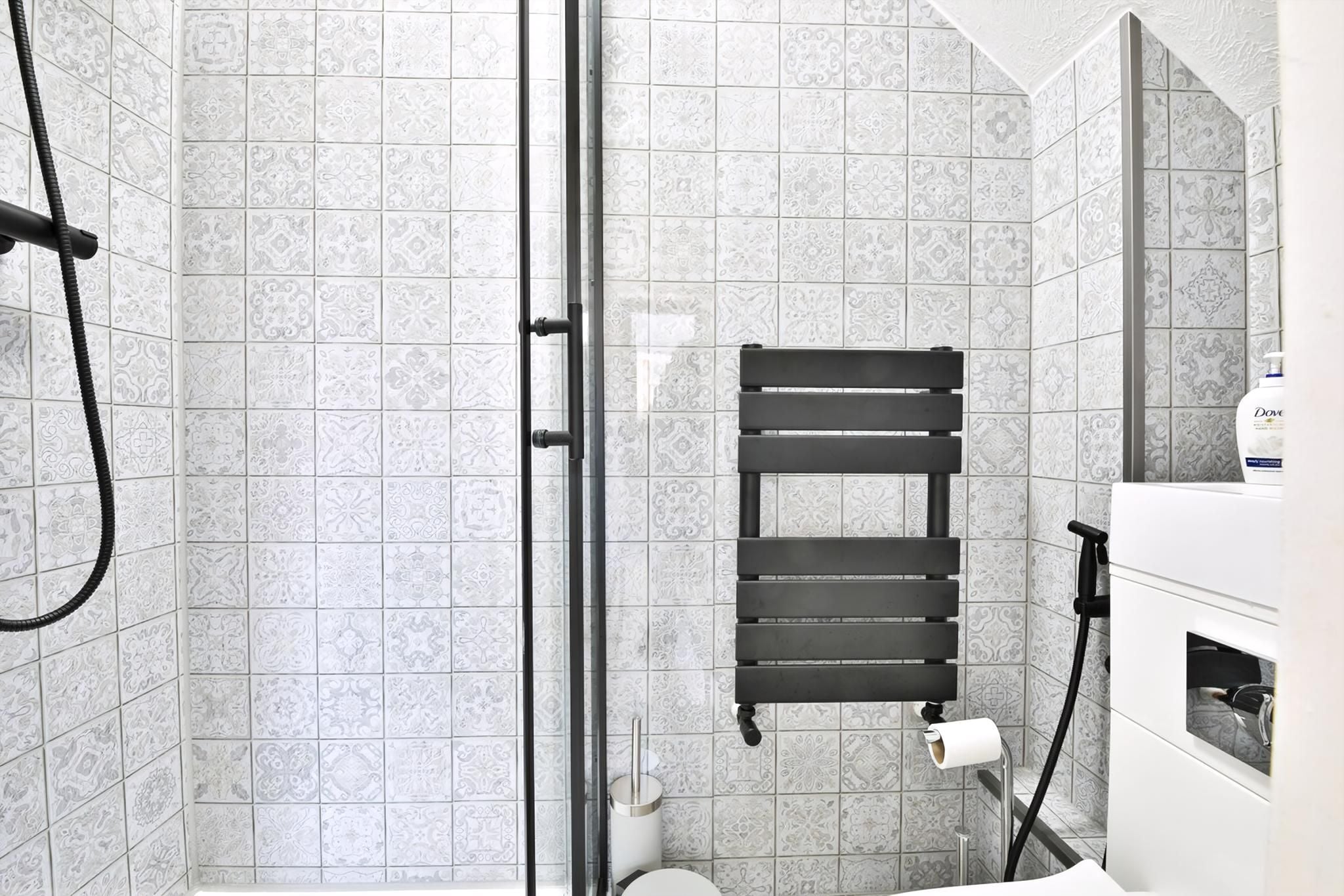 A bathroom with patterned tiles, a glass shower enclosure, a towel rack, and a toilet.