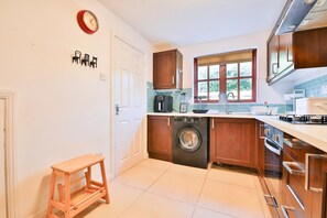 A compact kitchen with a washing machine, a coffee maker, and a window. - Homely 5 Bed House - 15 Mins to Cardiff City (Cardiff)