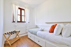 Un dormitorio con cama, ventana con cortinas, un banco y un radiador.
