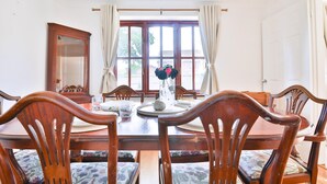 Une salle à manger avec une table en bois, des chaises, un vase de fleurs et une fenêtre avec des rideaux.