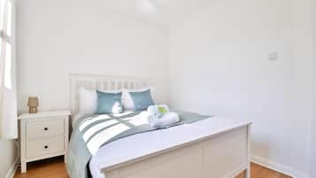 A white bedroom with a bed, nightstand, and lamp.