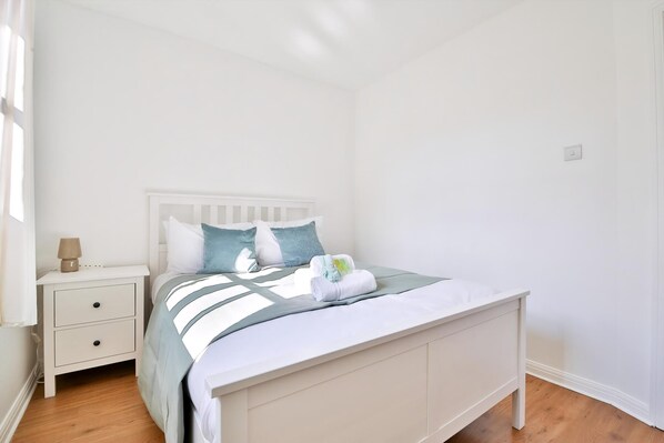 A white bedroom with a bed, nightstand, and lamp.