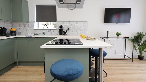 A modern kitchen with green cabinets, a white countertop, and a built-in stove.