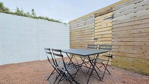 An outdoor patio with a table and chairs, a white wall, and a wooden fence.