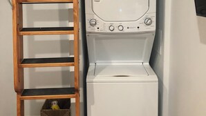 Een kleine wasruimte met een ingebouwde wasmachine en droger, een houten ladder en een plankunit.
