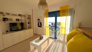 A modern living room with a TV, white cabinets, a bench, and a sofa with yellow cushions. - 25 - Livingtarifa The Island (Tarifa)