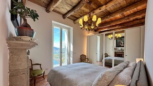 A bedroom with a bed, a chandelier, a mirror, and a view through a window. - Nestled on the hillside of Cernobbio, this enchanting 1608 structure, once a Convent, has undergone a meticulous restoration, now comprising three self-contained apartments. This unit with its tasteful décor, ensures a harmonious blend of style and comf (Cernobbio)