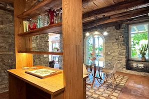 A rustic interior with a wooden table, stone walls, and a view of greenery outside.