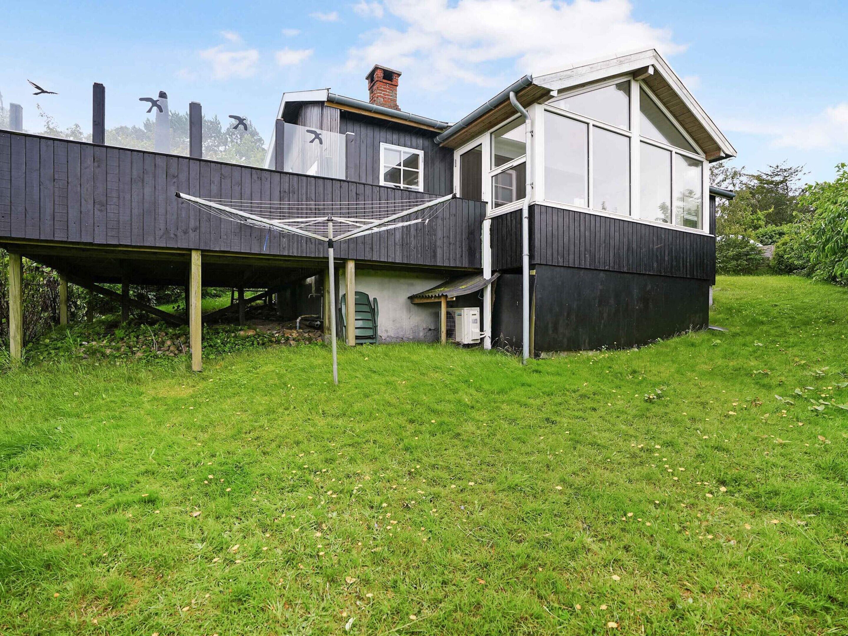A modern house with a flat roof and large windows, situated on a grassy hill.