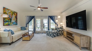A spacious living room with a large flat-screen TV, a ceiling fan, and a painting on the wall. - Waterfront Cape Coral Home: Views & Birdwatching (Cape Coral)