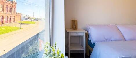 A hotel room with a bed, a bedside table, and a window offering a view of a building and a street.