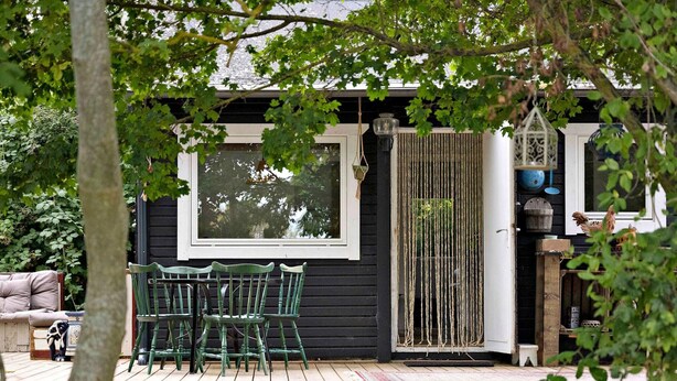 A wooden deck with green chairs and a table, a window, and a door with a rope curtain.