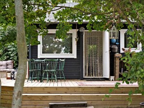 A wooden deck with green chairs and a table, a window, and a door with a rope curtain.