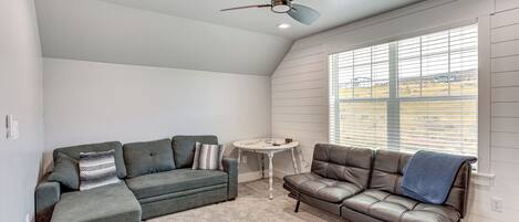 A room with two sofas, a ceiling fan, a small table, and a window with blinds.