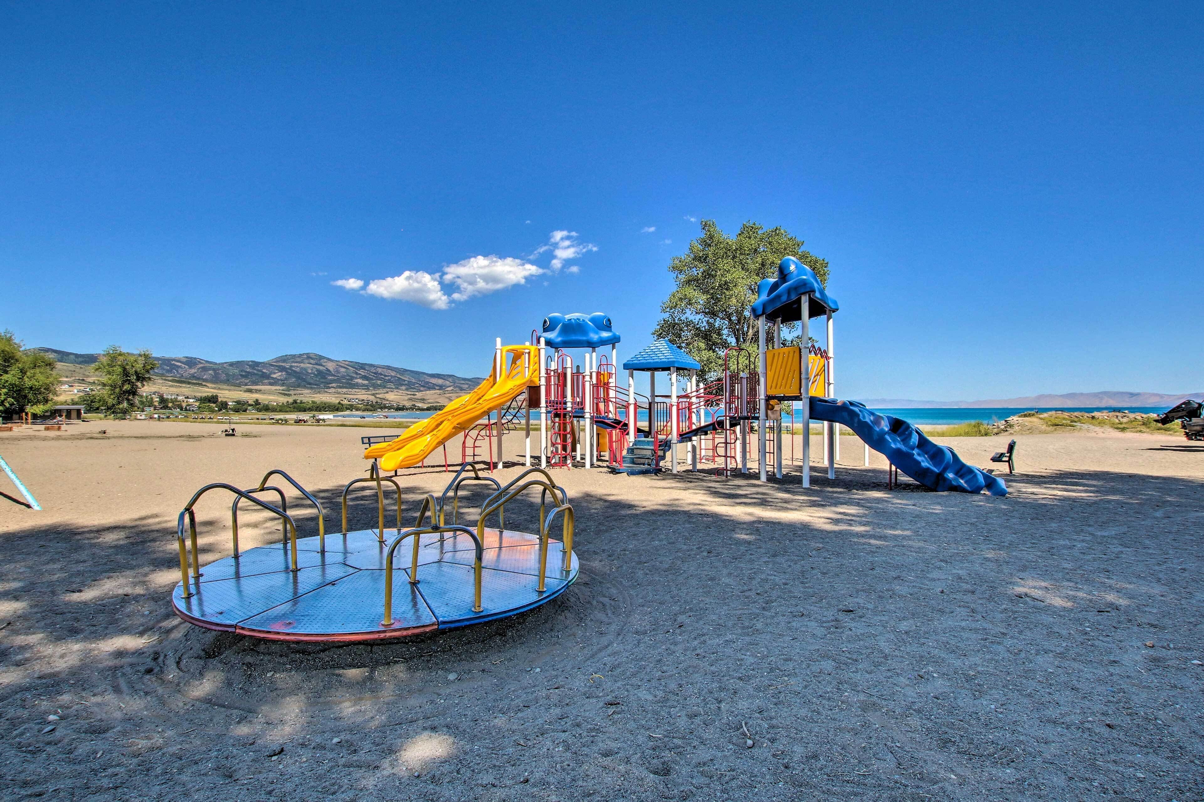 A playground with slides and a rotating platform, set against a clear sky and distant mountains.