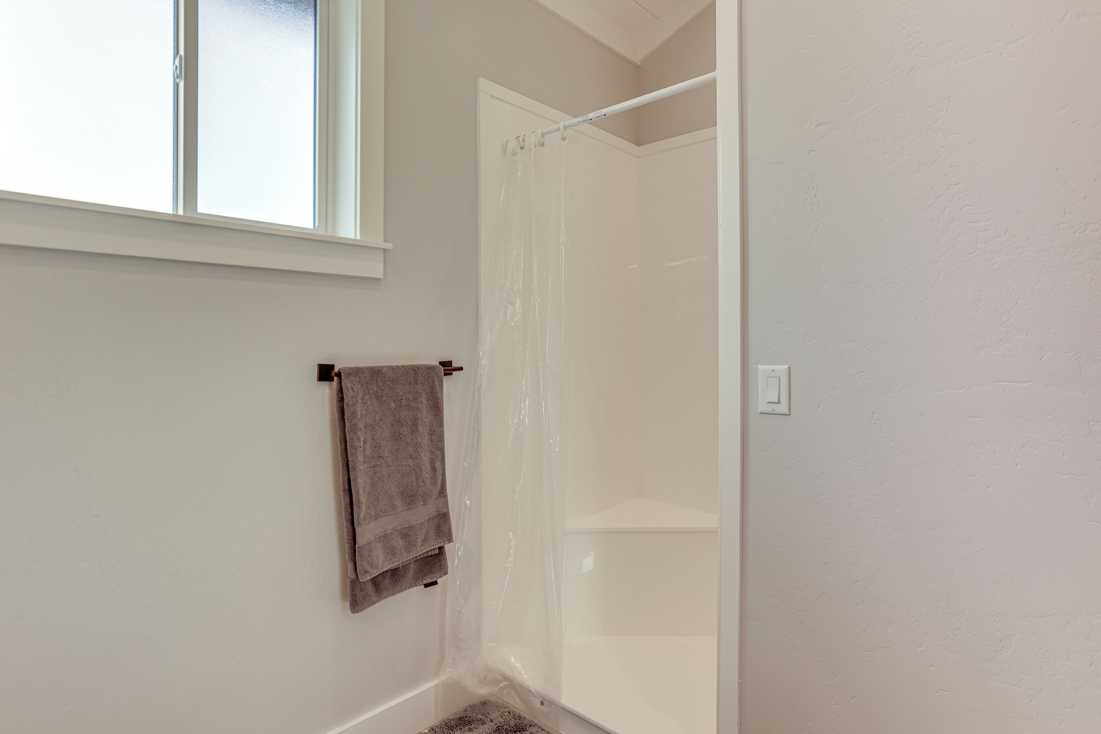 A bathroom with a shower, a towel hanging on the wall, and a window providing natural light.