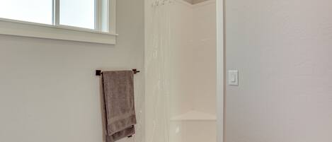 A bathroom with a shower, a towel hanging on the wall, and a window providing natural light.
