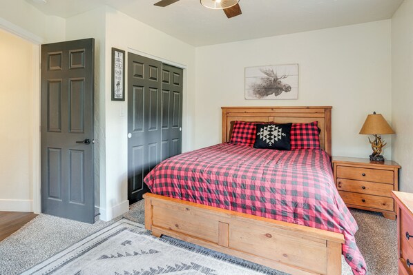 A bedroom with a wooden bed, a gray door, a wooden nightstand, and a wall-mounted lamp.
