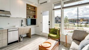 Eine moderne Küche mit Einbauofen, einem Essbereich mit einem grünen Stuhl und Blick auf einen Parkplatz durch große Fenster.